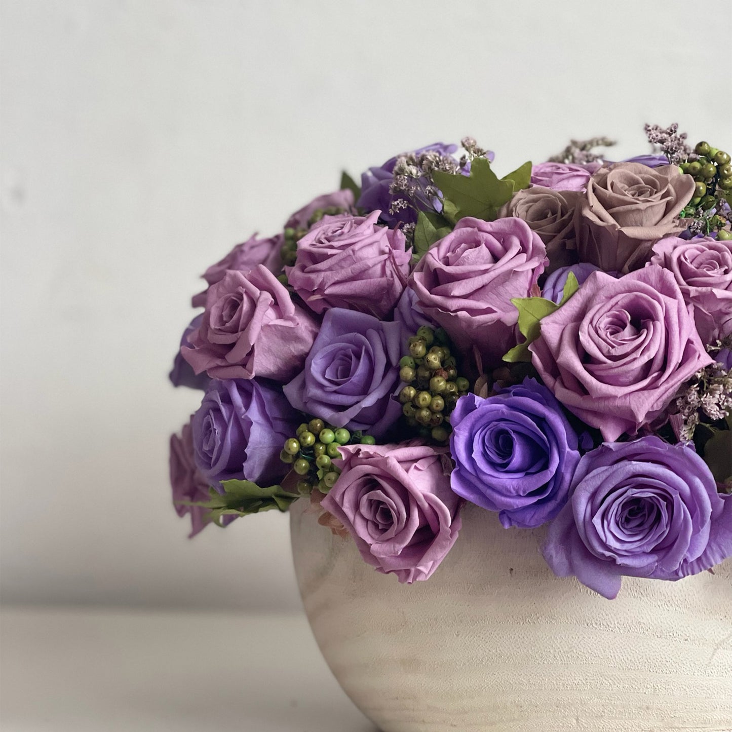 Amethyst Cloud arrangement showcasing layered purple roses, green pepperberry, and statice