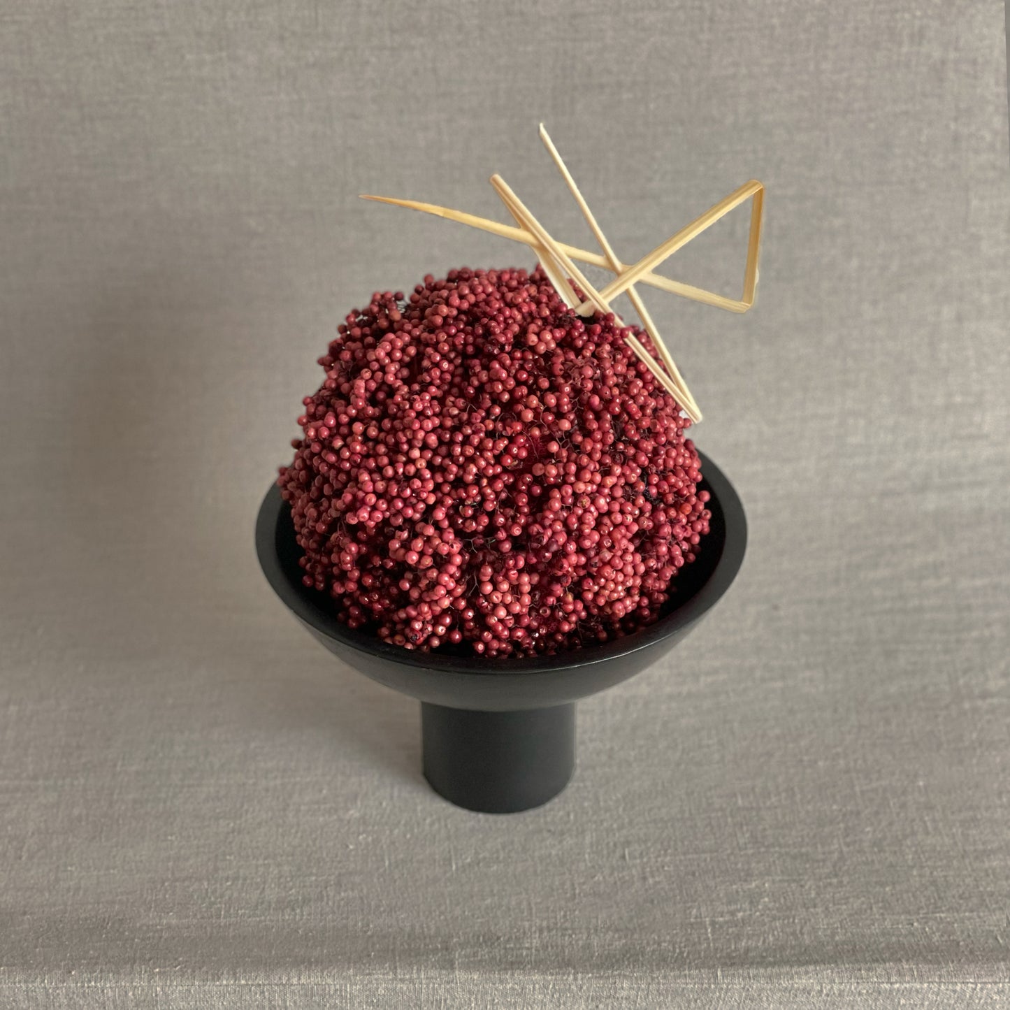 Japanese-inspired floral arrangement with preserved pepperberry and lily grass accent in a modern black bowl.