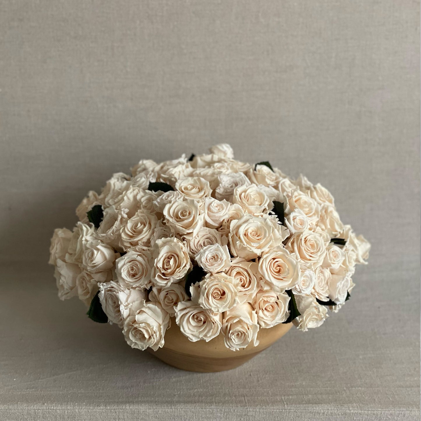 Elegant preserved ivory roses arranged in a sleek teak wood bowl for a modern floral centerpiece.