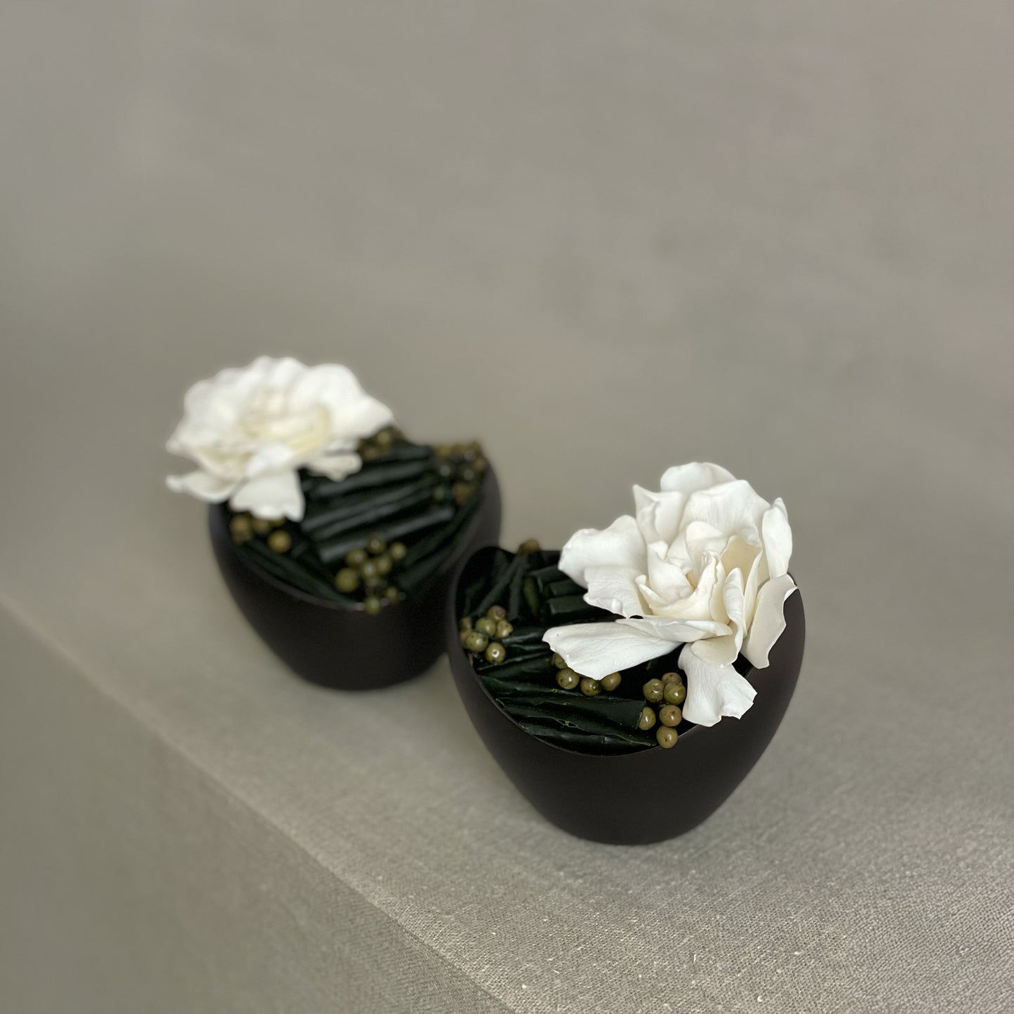 Elegant preserved gardenia with green California pepperberry, displayed in a black minimalist vase, perfect for a bedside or bookshelf accent.