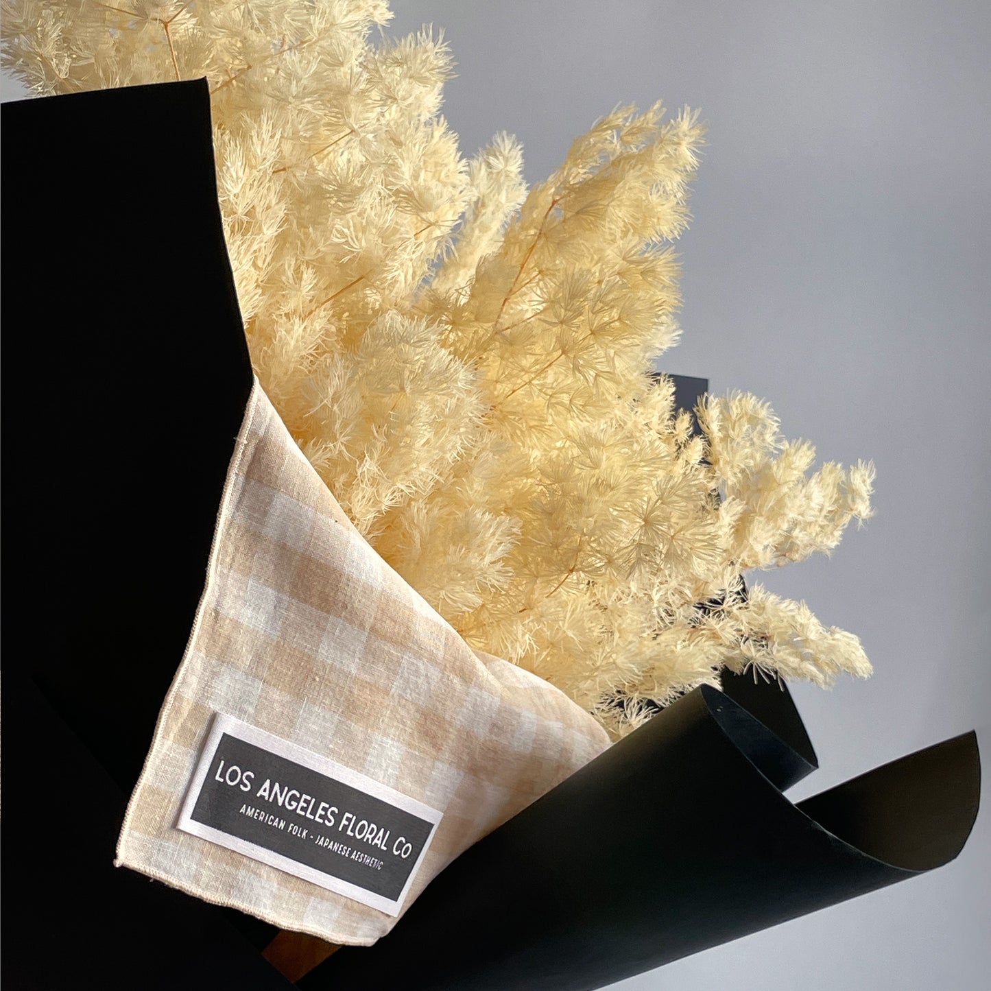Close-up view of preserved white Ming fern branches, artfully bundled and wrapped in a furoshiki cloth, highlighting the soft, airy feel of the fern leaves.