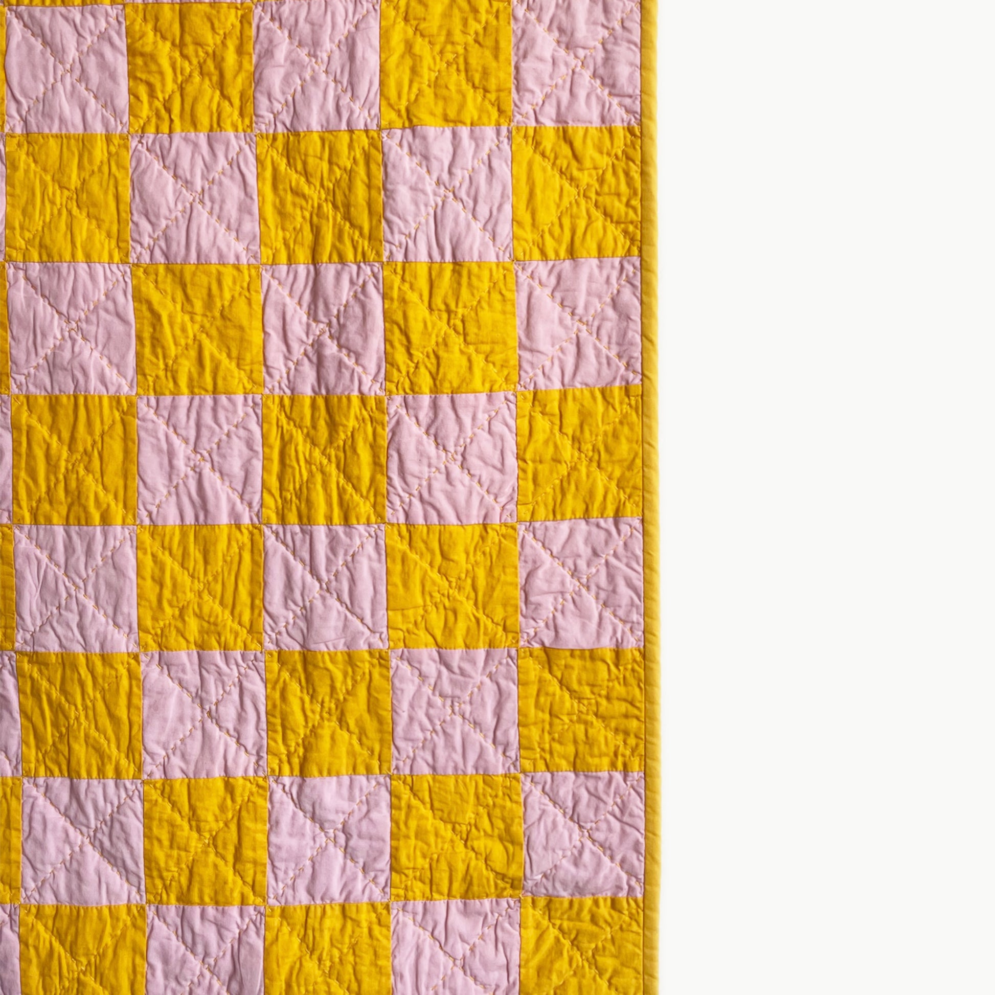 Close-up of the golden yellow and pink checkerboard quilt pattern by Los Angeles Floral Company, showcasing Sashiko-style hand-stitching.