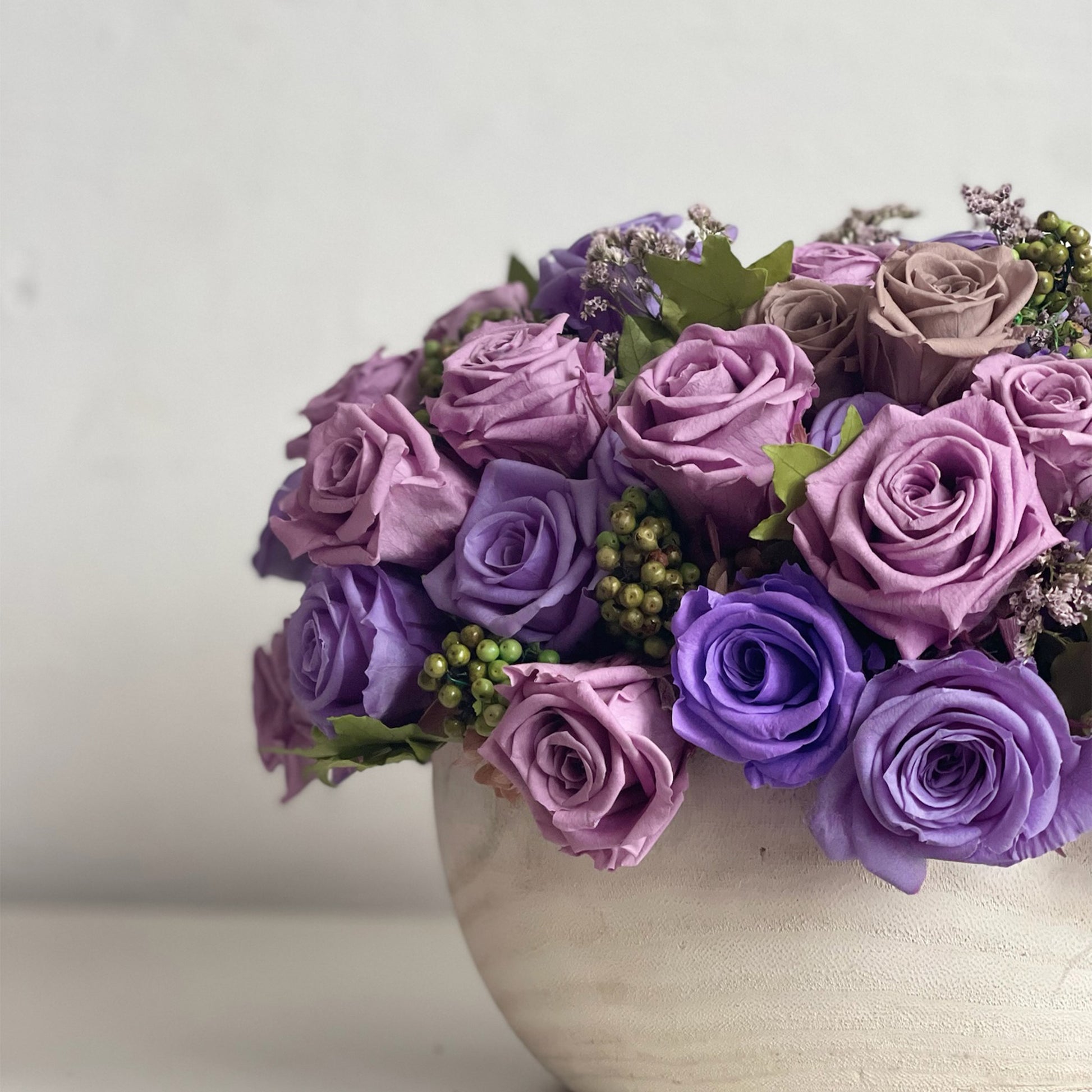 Amethyst Cloud arrangement showcasing layered purple roses, green pepperberry, and statice