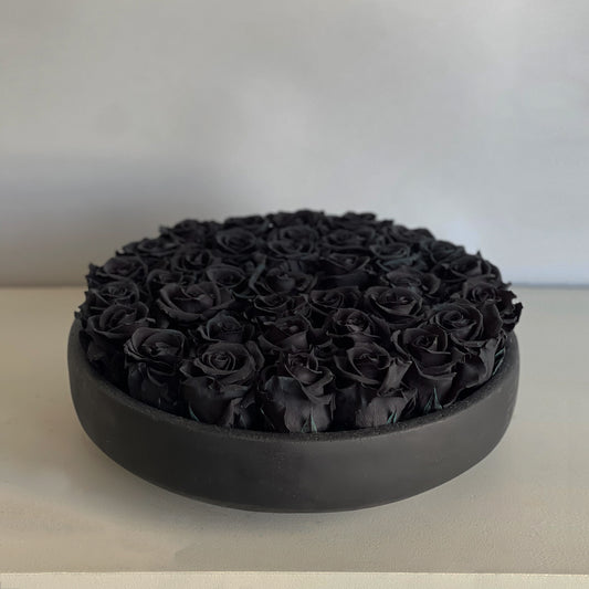 A close-up of the Black Rose Serene arrangement, featuring preserved black roses artfully arranged in a round, matte black ceramic bowl, offering a striking and dramatic centerpiece.