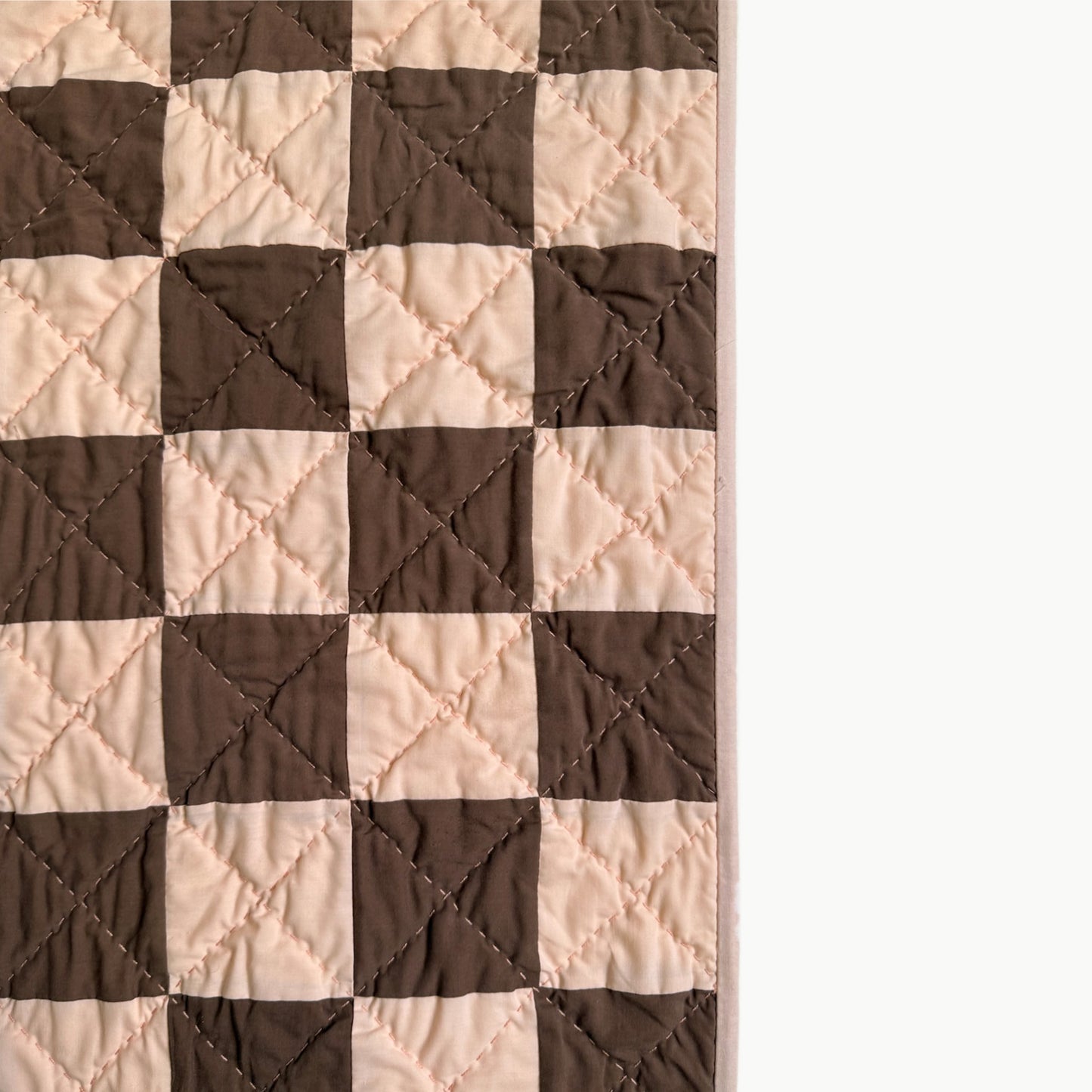 Close detail of peach and brown checkerboard quilt blocks with hand quilting from the Deadwood Dick Twin quilt.