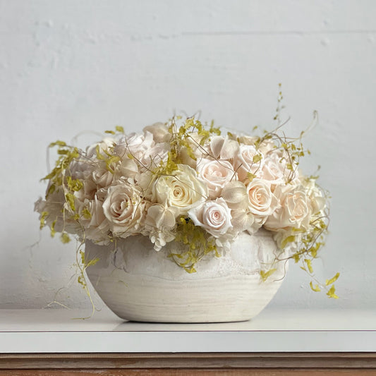 Delicate Dawn preserved floral arrangement with ivory roses, lantern pods, and vine in a whitewashed bowl.