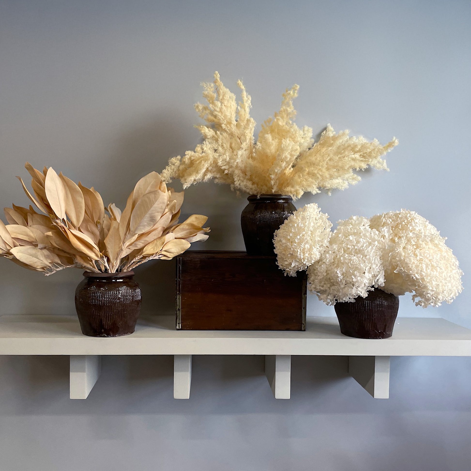 A preserved botanical arrangement from the 2024 Holiday Ginger Jar Series, featuring White Hydrangeas, Golden Magnolia, or Bleached Ming Fern, each displayed in its own handcrafted ceramic ginger jar.