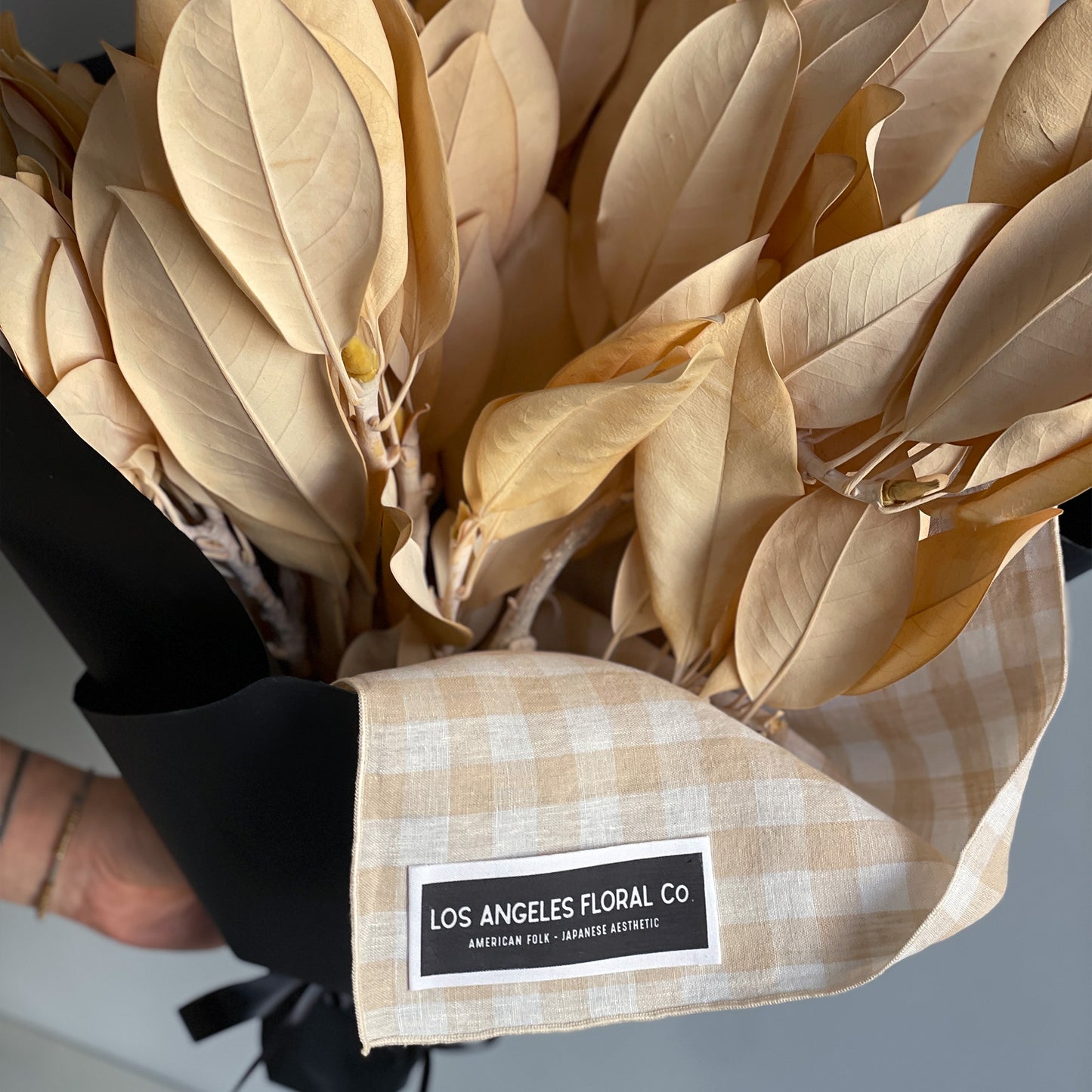 Close-up view of preserved golden magnolia branches, artfully bundled and wrapped in a furoshiki cloth, highlighting the delicate texture and elegant presentation.