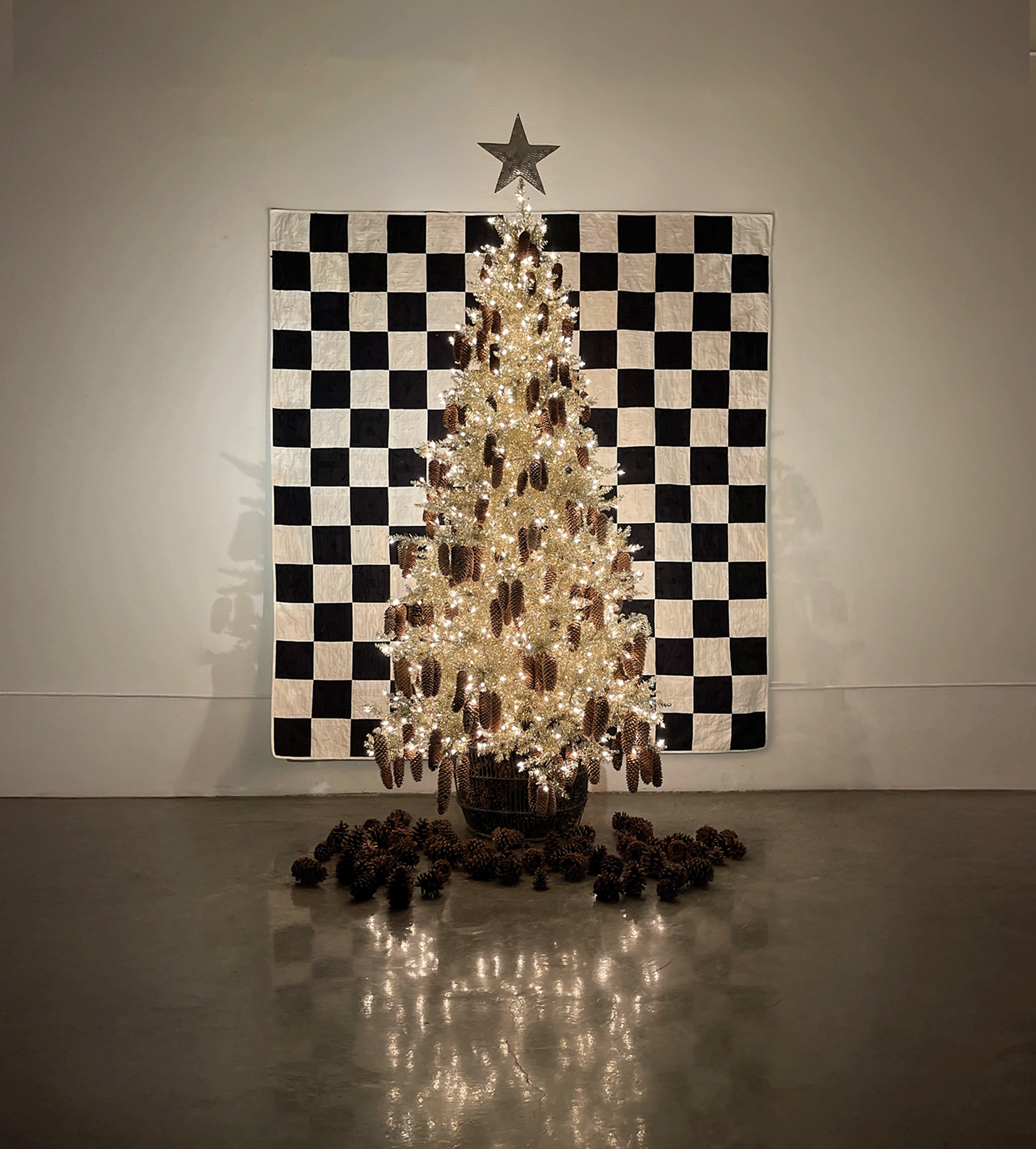 Holiday tree adorned with sparkling lights and pinecones, set against a black-and-white checkered quilt backdrop in a cozy, modern studio space.