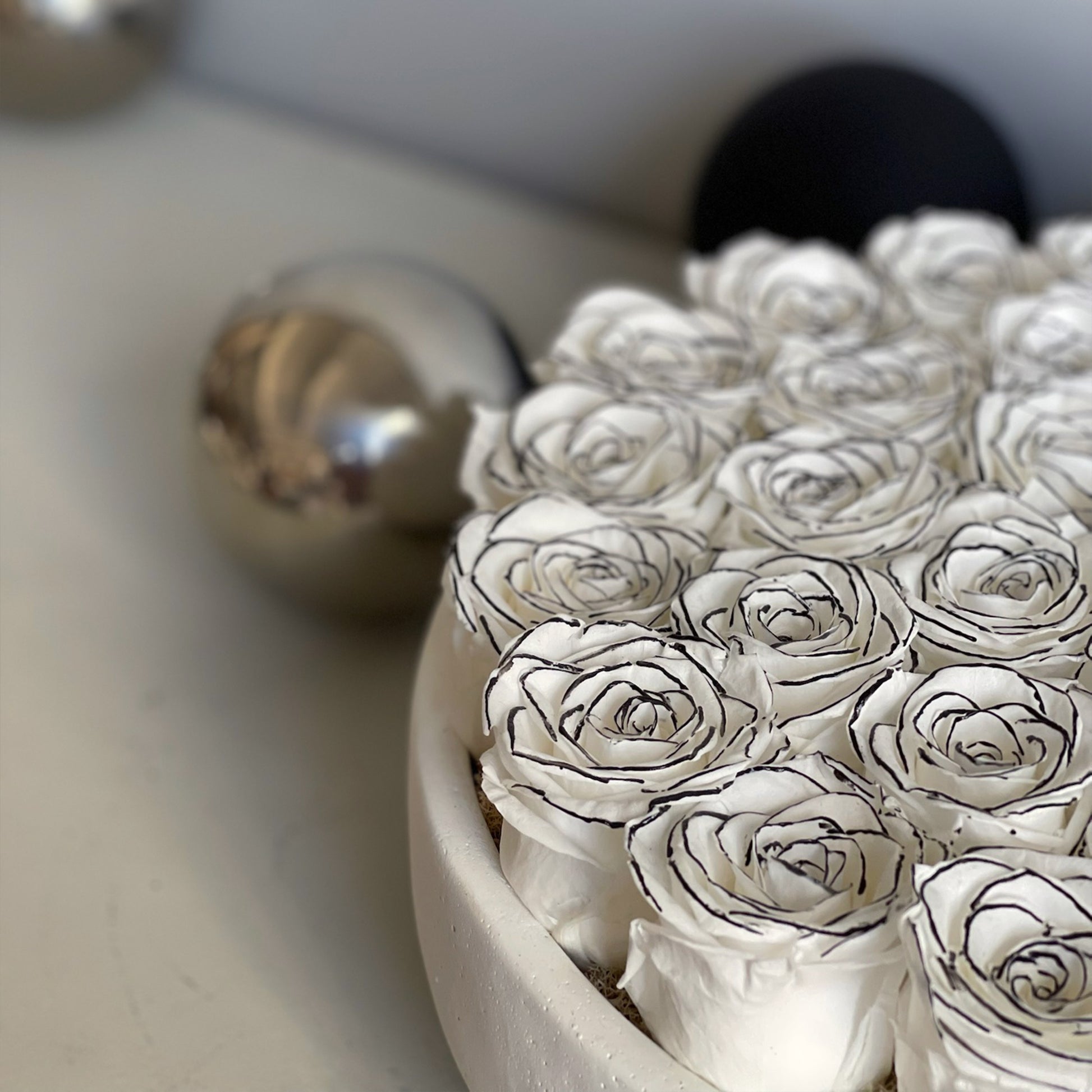 Close-up view of preserved ivory roses with hand-drawn black lines, showcasing the intricate detail of each petal, in a sleek, modern.