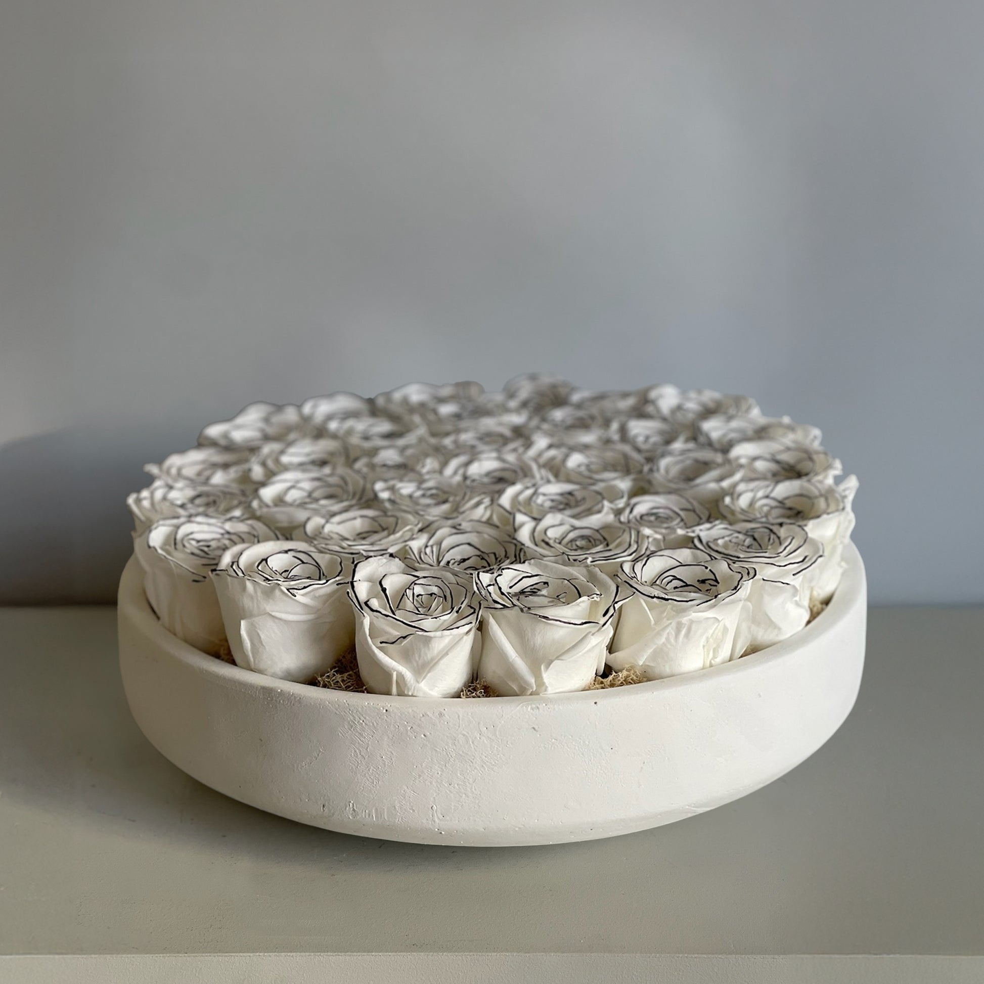 Preserved ivory roses with hand-drawn black line details, displayed in a minimalist ceramic bowl, evoking Art Deco style.