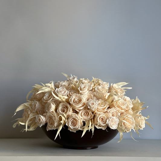 A preserved ivory rose and willow eucalyptus arrangement in a handcrafted walnut-toned wooden bowl, showcasing a timeless, serene design.