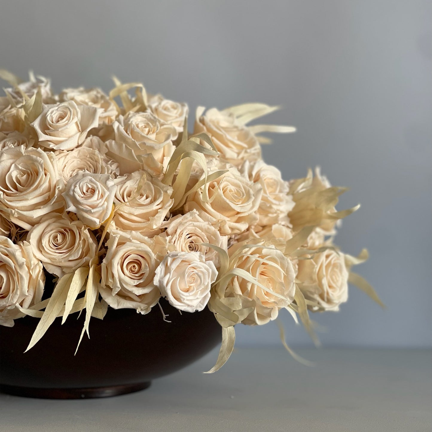 Close-up of the preserved ivory roses and willow eucalyptus in the walnut-toned wooden bowl, capturing the natural textures and minimal elegance.