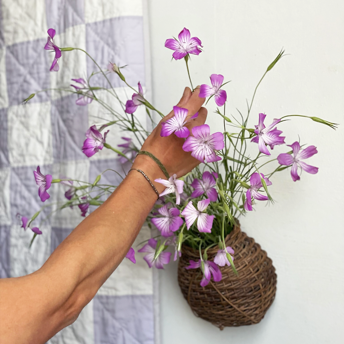 Keigo, co-founder of Los Angeles Floral Company, arranging delicate purple flowers against a quilt background on the Onko Chishin page within the Inspirations section.