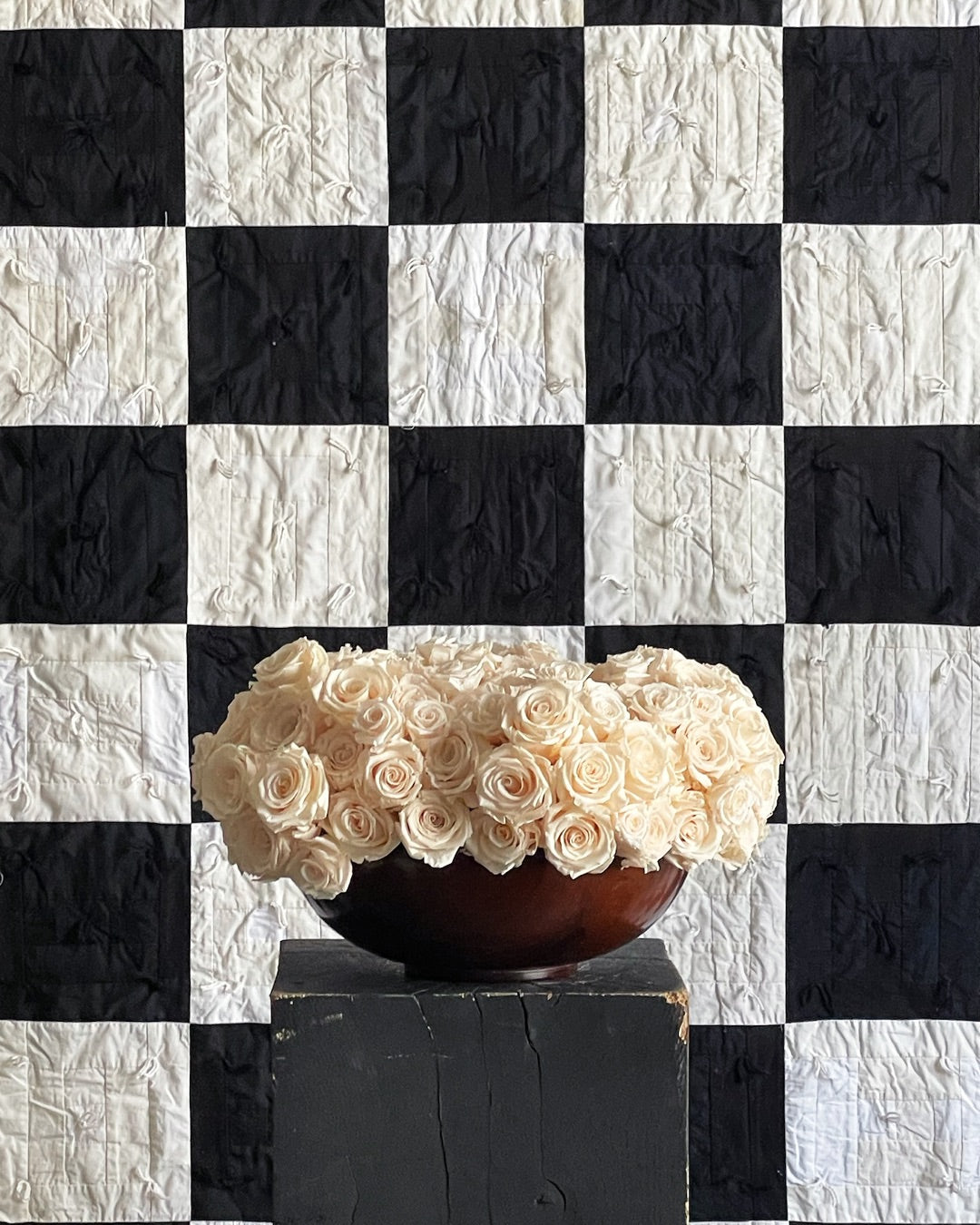 A display of preserved white roses set against a black and white checkerboard quilt backdrop, showcasing the fusion of floral artistry and textile craftsmanship by Los Angeles Floral Company.