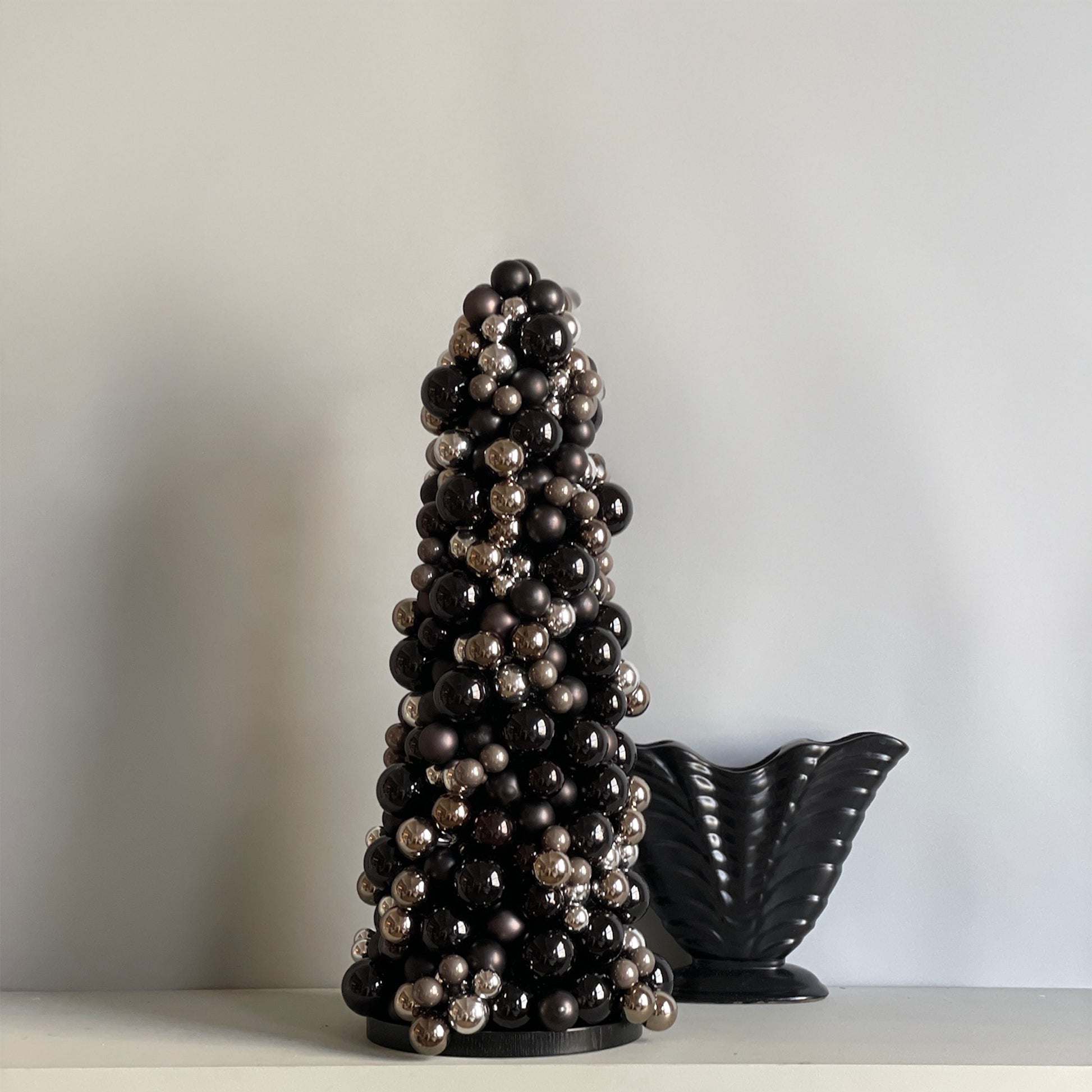 A striking black and chrome glass bauble cone tree, crafted in a bold, sculptural design, inspired by the glamour of the 1920s Art Deco era, with a sleek black wood base.