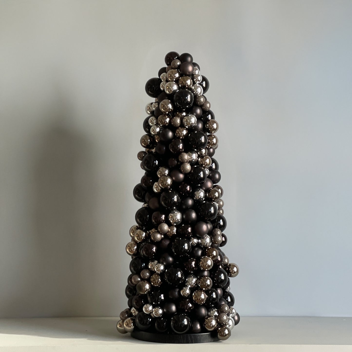 Side view of the Moonlit Noir glass bauble cone tree, showcasing its dramatic design with metallic gunmetal baubles and a refined black wood base.