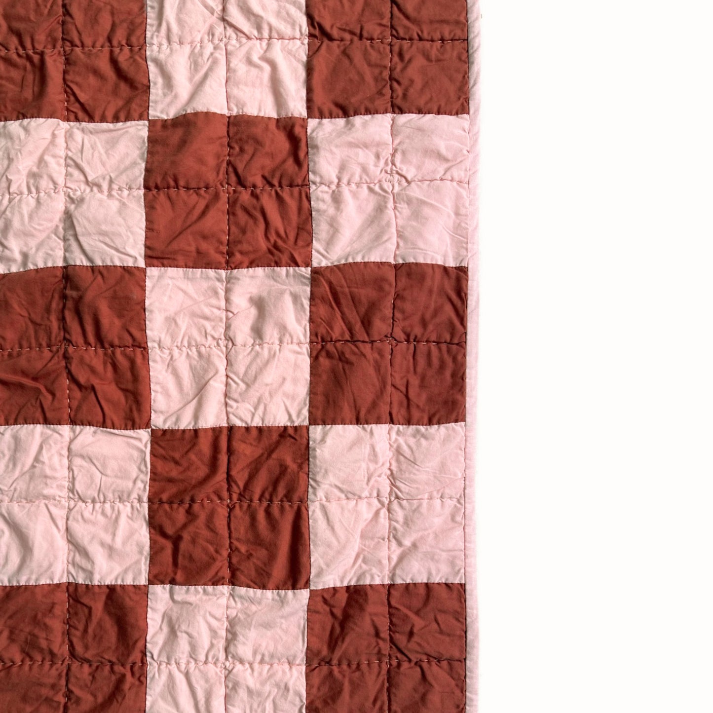 Close detail of pink and rust checkerboard quilt blocks with hand quilting from the Nat Love throw.