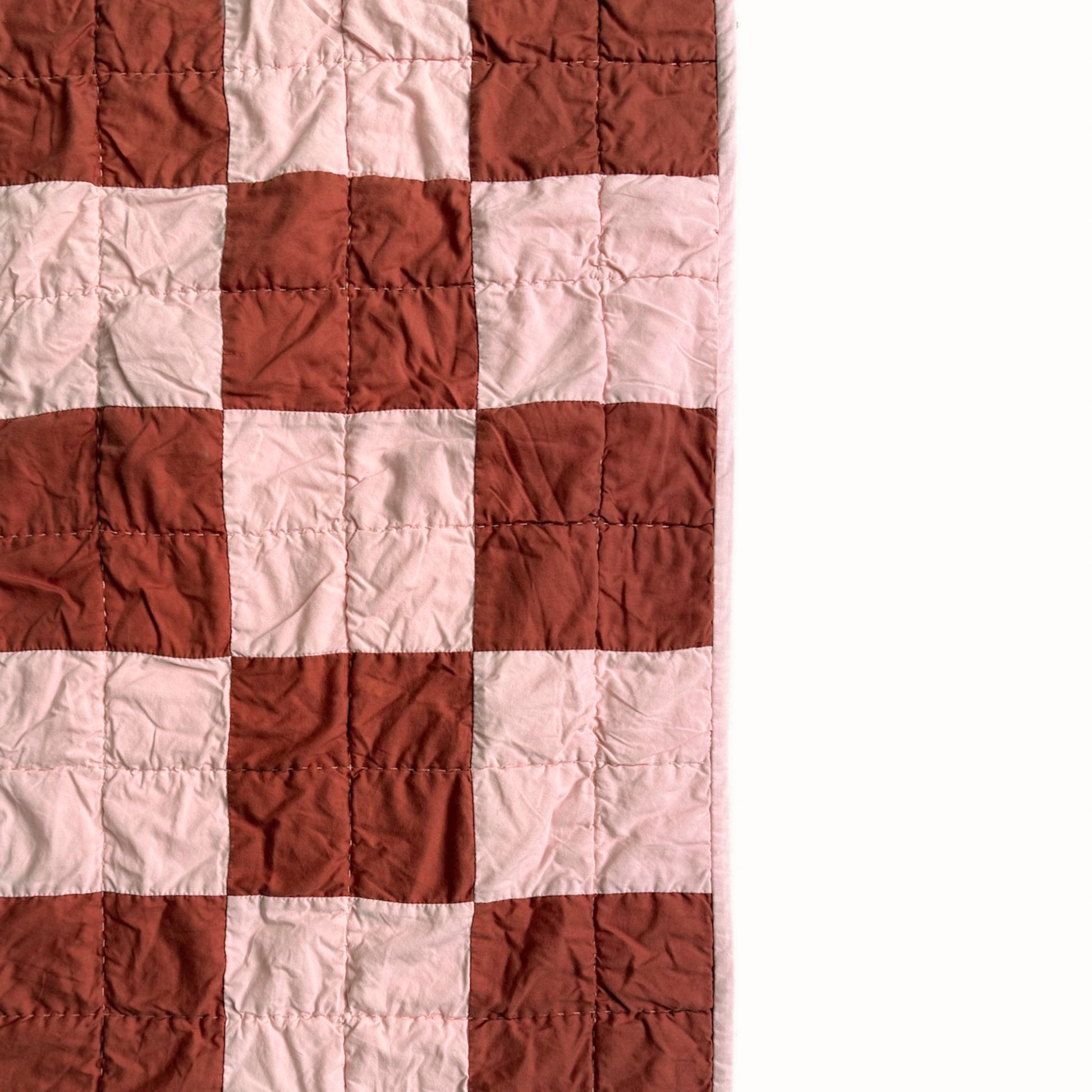 Close detail of pink and rust checkerboard quilt blocks with hand quilting from the Nat Love throw.