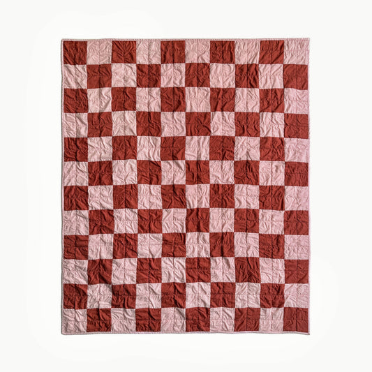Full view of pink and rust checkerboard hand-quilted throw quilt inspired by Nat Love, Showman Series Act One.