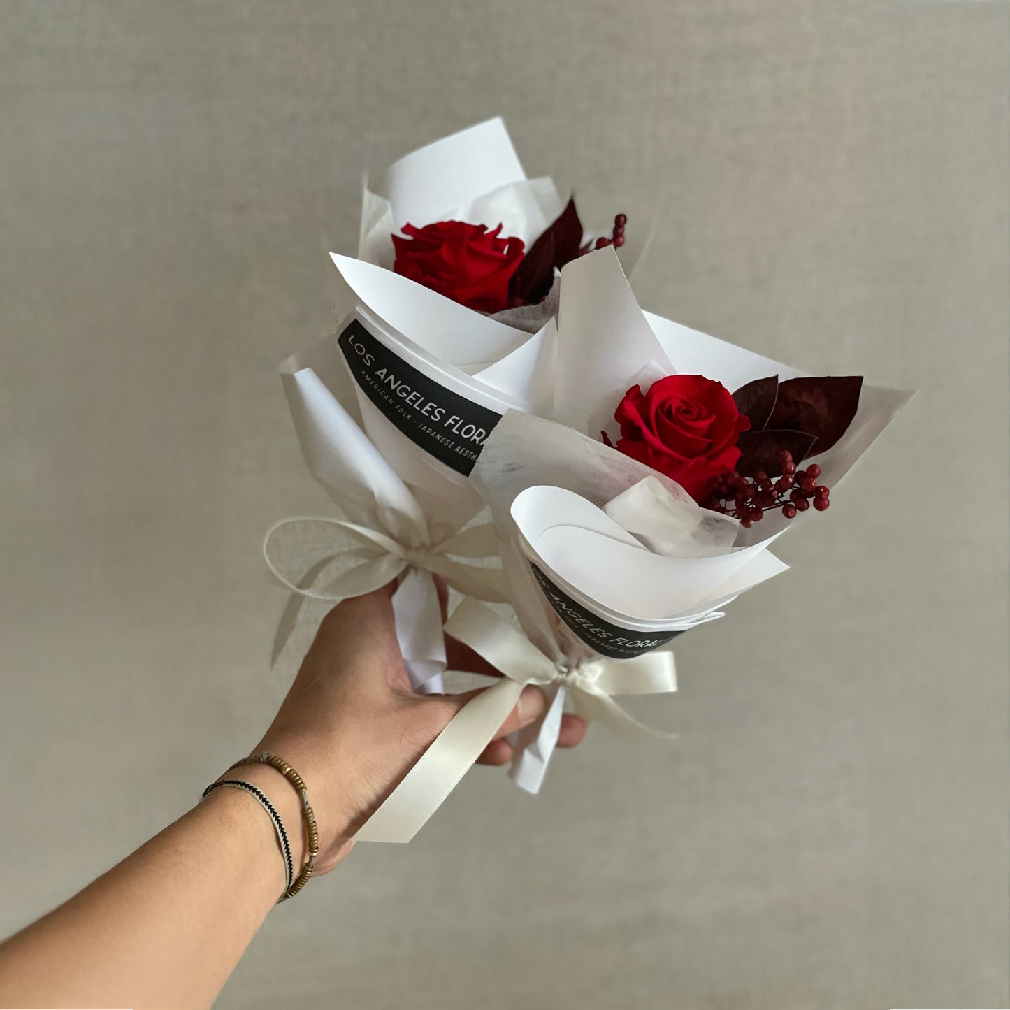 Preserved red rose mini bouquet accented with California pepperberry and velvet leaves, beautifully wrapped in elegant white paper with a ribbon bow.