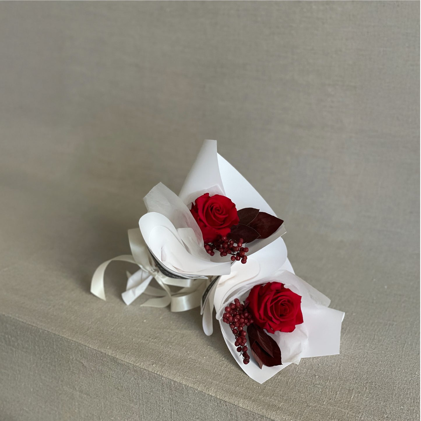 Stylish and modern preserved rose mini bouquet featuring red hues, white wrapping, and a classic bow.