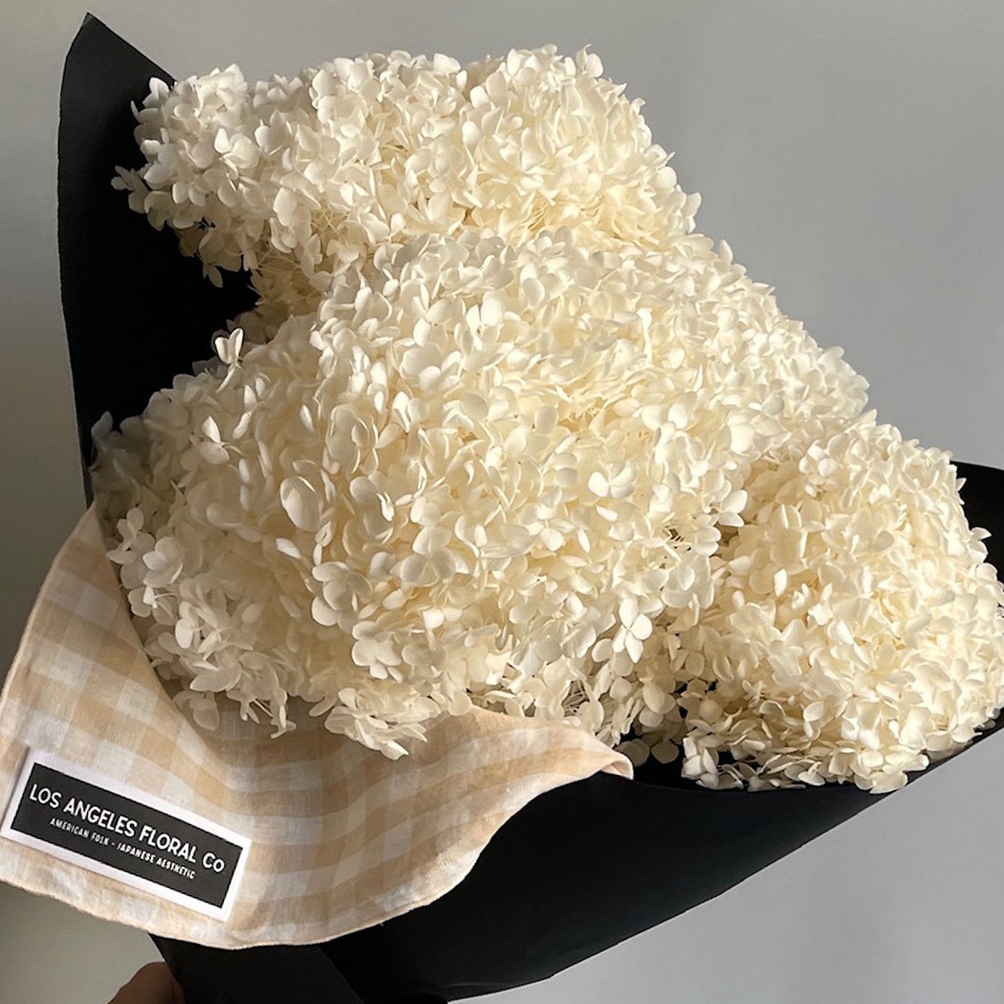 Closed up of a bundle of preserved white hydrangea blooms wrapped in furoshiki-inspired cloth, showcasing their soft texture.