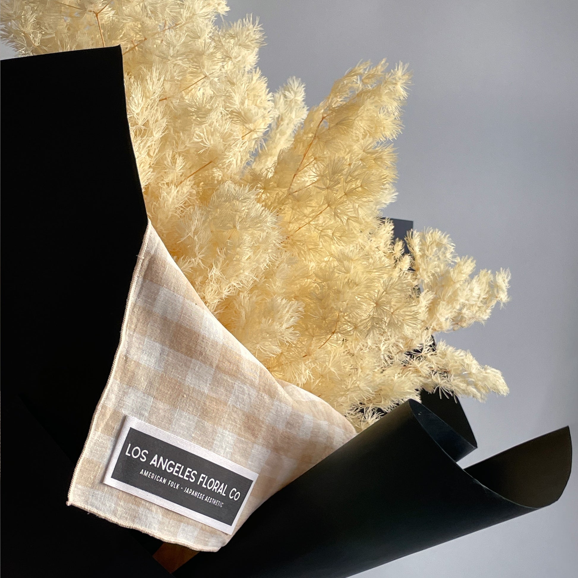 Close-up view of preserved white Ming fern branches, artfully bundled and wrapped in a furoshiki cloth, highlighting the soft, airy feel of the fern leaves.