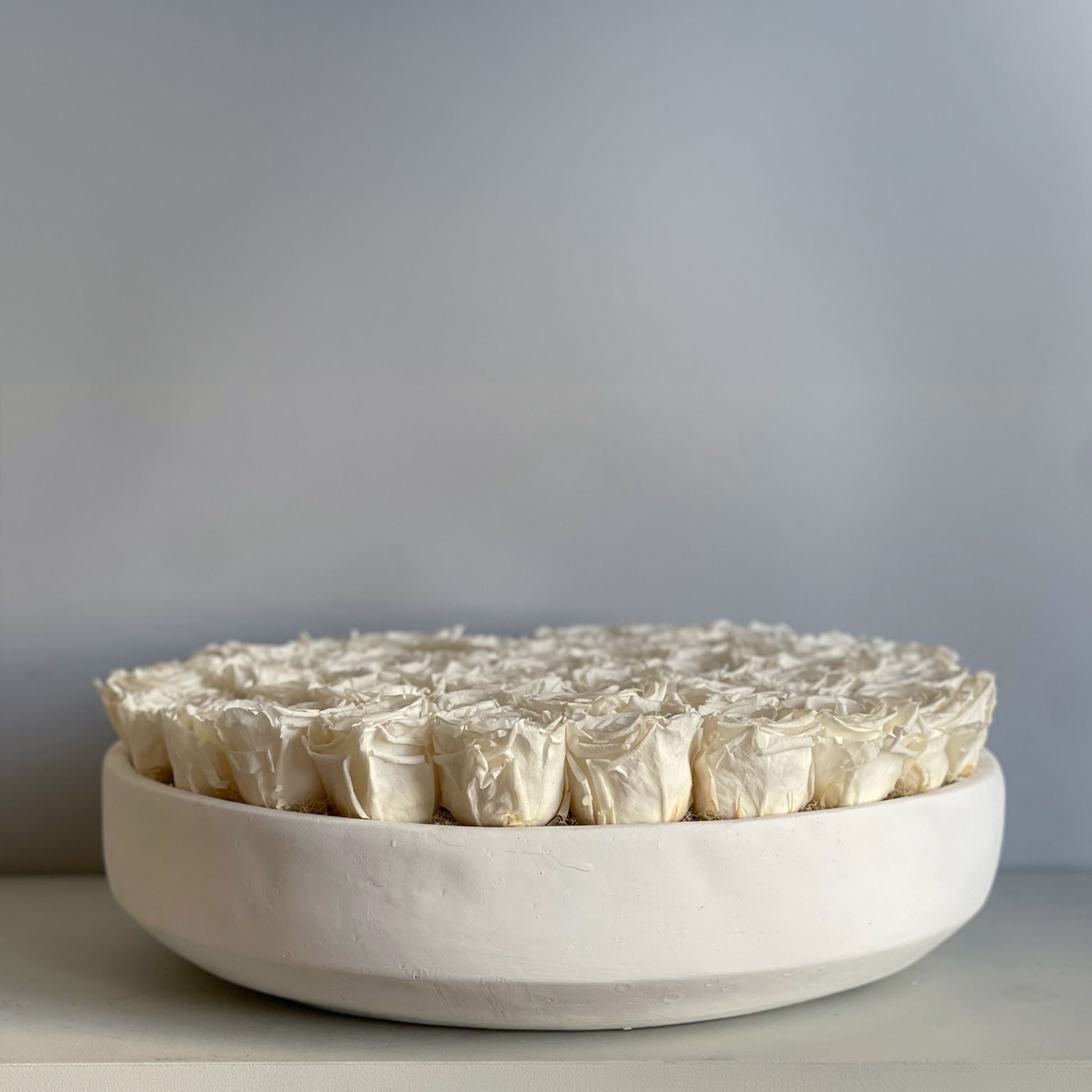  A side view of the white rose serene arrangement, revealing the depth and texture of the preserved white roses in their sleek, round base.